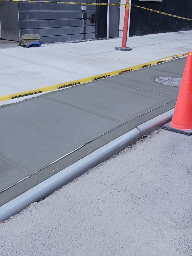 Newly poured concrete sidewalk with caution tape and orange cones blocking access